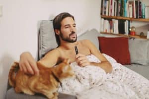 homme allongé dans son lit avec son chat fumant une cigarette électronique